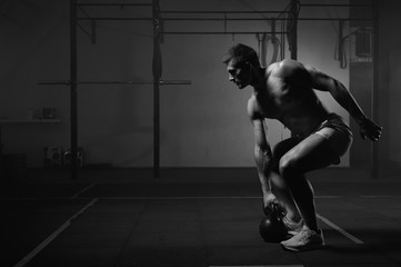 Muscular man working out with kettlebell in gym