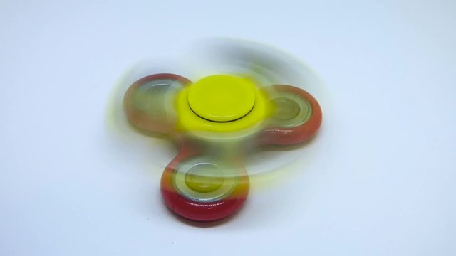 Bright yellow and red fidget finger spinners on white background. Stress relieving toy rotating fast and gradually stops.