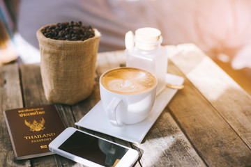 Cup of hot coffee with the telephone placed on a wooden table.