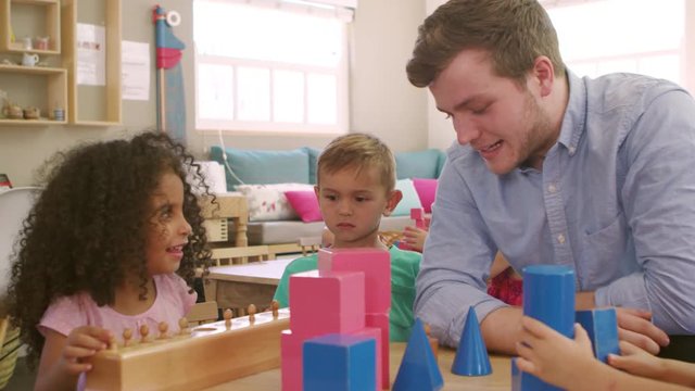 Teacher And Pupils Using Wooden Shapes In Montessori School