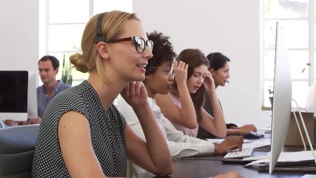 A row of women using phone headsets in an open plan office