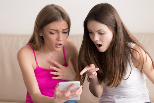 Two cute young girlfriends looking on digital tablet screen with surprise feeling excited because of amazing offer, sale in online shop, shocked with discounts in Internet store, found something great