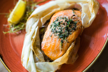 On a wooden board, on a red plate a salmon steak, in craft paper, lemon, rosemary, spices, two...