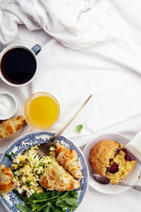Breakfast in bed. Scrambled eggs with cheese croissants, raspberry muffin and black coffee. Morning treat concept. Composition with copy space.