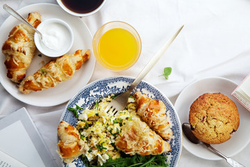Breakfast in bed. Scrambled eggs with cheese croissants, raspberry muffin and black coffee. Lazy morning concept. Flat lay with copy space.