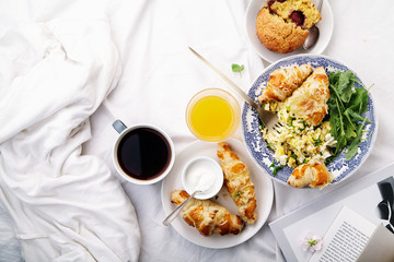 Breakfast in bed. Scrambled eggs with cheese croissants, raspberry muffin and black coffee. Morning treat concept. Composition with copy space.