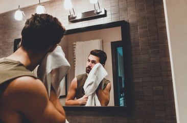 Reflection of young man in bathroom mirror looking on his face