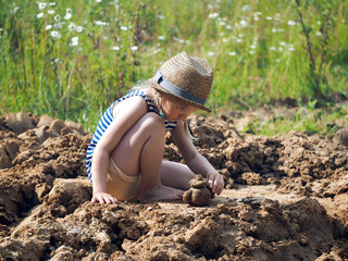 Little girl sculpts out of clay. A lot of dirt, funny baby