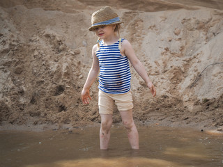 Happy little girl playing in a big puddle of sand quarry