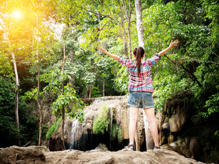 Naklejka na ściany i meble Journey vacation tourist concept - Happy young female traveler open arms with happiness in front of beautiful waterfall with nature. Having a great vacation for hiking. film effect