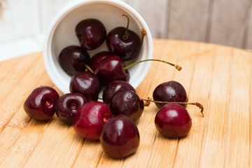 Bowl of ripe black cherries spilled on wooden tab