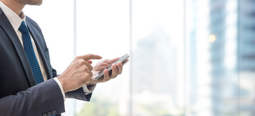 Business man using smart phone on window with city building background and copy space.