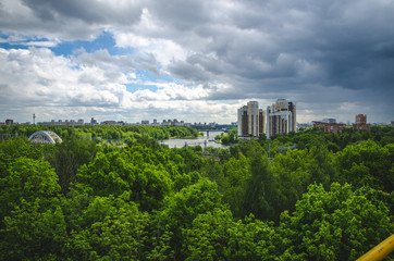 Fototapeta premium KHIMKI, RUSSIA - JUNE 1, 2017: The view from the Ferris wheel at green park. Under construction skyscrapers on the horizon. The sense of height above the trees.