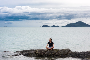 Portrait of a man with sitting on the rock with sea, mountain and cloud