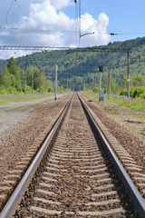 Railway in the forest area.
One railroad goes ahead, in perspective. The forested mountain is in the background. Siberia, Russia.
