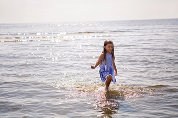baby girl in a striped dress and runs to the sea the ocean