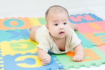 Portrait of a little adorable infant baby girl lying on the tummy on colorful eva foam indoors