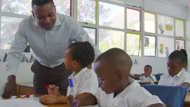 Teacher stands helping elementary school kids at their desks