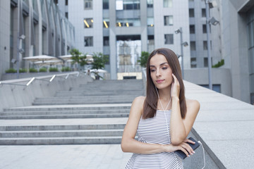 Beautiful brunette woman listening music from a smartphone on the background of an office building.