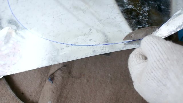 Hands of technician using hard scissor to cutting a sheet of alu zinc for circle layout shape