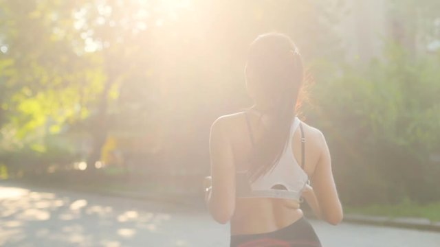 Handsome woman runing through the park in the morning during sunrise. View from the back.