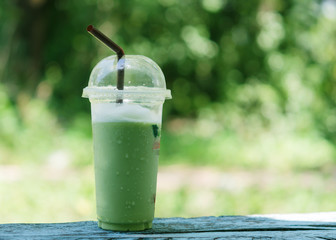 Green tea is spun in a glass placed on a wooden floor. The natural light bokeh is the background...