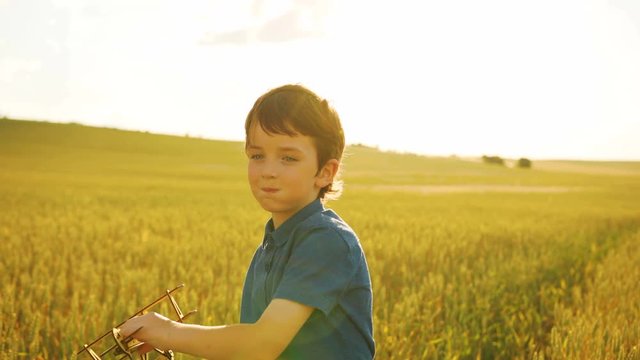 Young beatiful boy playing with wooden plane in the field at hte sunset background.