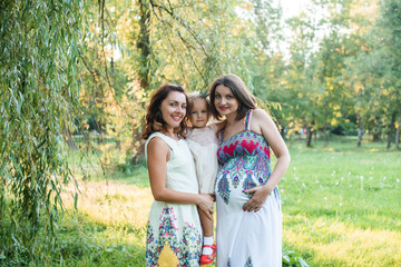young beautiful pregnant woman walking in the park With a little daughter And sister on a sunny summer day