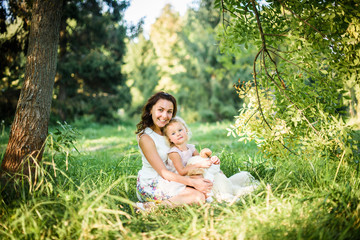 Naklejka na ściany i meble young beautiful pregnant woman in the park With a little daughter And sister on a sunny summer day
