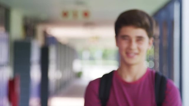 White teenage boy walks into focus in high school corridor