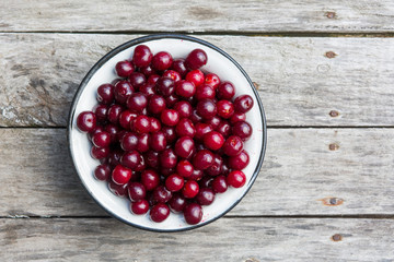 Cherry in a white bowl on a old wooden texture with rasty nails. Top view.