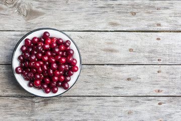 Cherry in a white bowl on a old wooden texture with rasty nails. Top view.