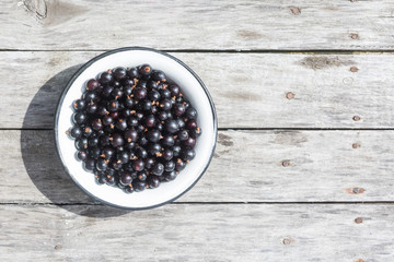 Black currant in a white bowl on a wooden texture with rusty nails. Top view. Copyspace.