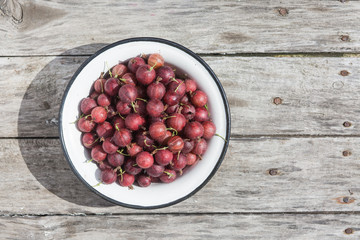 Gooseberry in a white bowl on a wooden texture with rusty nails. Top view.