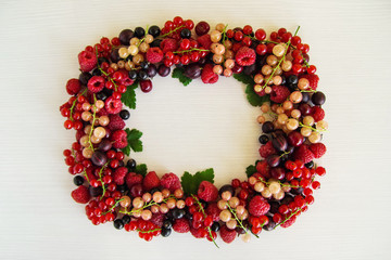 Frame from mixed summer berries on the white wooden background, top view.