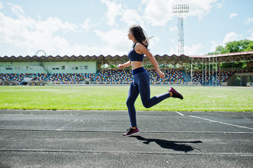 Fototapeta premium Portrait of a strong fit girl in sportswear running in the stadium.