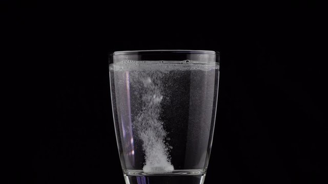 Effervescent antacid tablet in glass of water on black background
