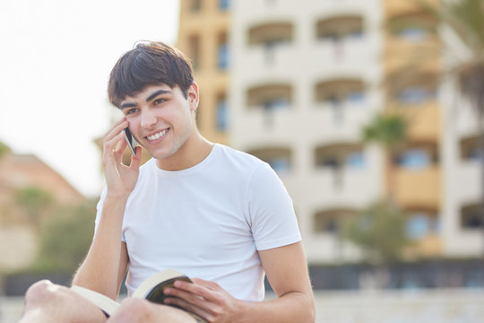 Young happy man talking on mobile and holding book