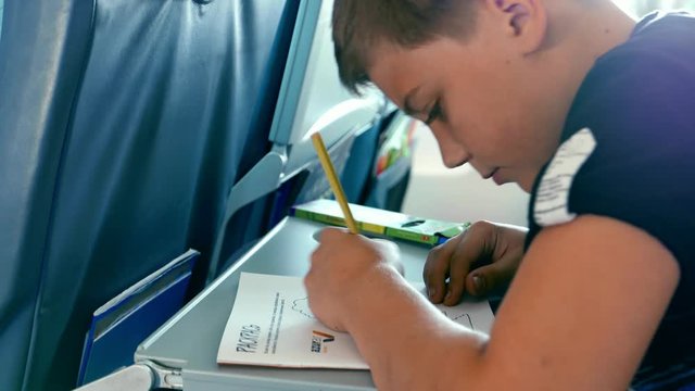 Flight, travel by aircraft. Boy teenager child paints in the airplane interior