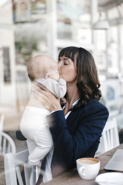 Businesswoman in cafe kissing her baby
