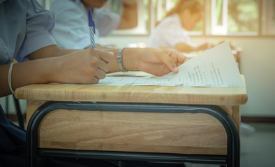 Fototapeta premium Asian School students in uniform taking examination and writing answer sheet in classroom, educational school, view of having exams in class on seat rows, Education system tests concept of Thailand