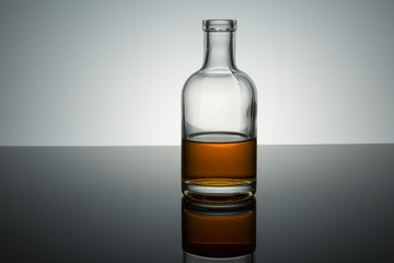 small clear bottle half full of burbon on reflective surface 