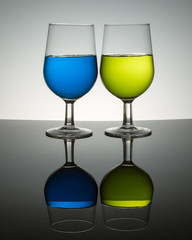 wine glasses on reflective surface blue yellow green liquid  half full