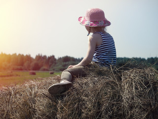 Naklejka na ściany i meble A small child sits on a haystack.