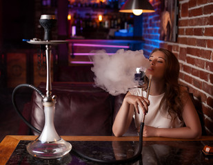 Beautiful girl in a white blouse smokes a hookah in the interior of the bar