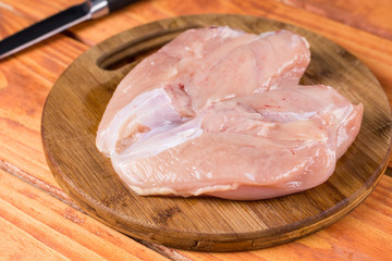 Raw chicken breasts fillet on the round kitchen wooden board