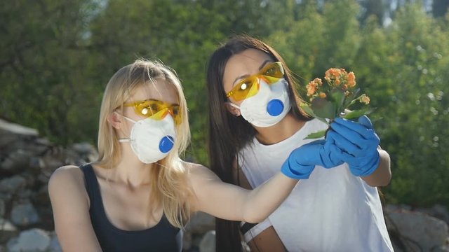 Girls in respirators and glasses hold a plant in their hands and examine it