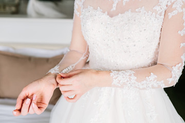 Bride is fasten sleeves on her dress, preparing for the wedding day