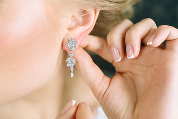 Elegant blonde bride putting on earrings, preparing for the wedding. Close-up