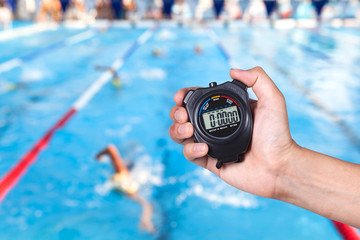 Stopwatch holding on hand with competitions of swimming background.